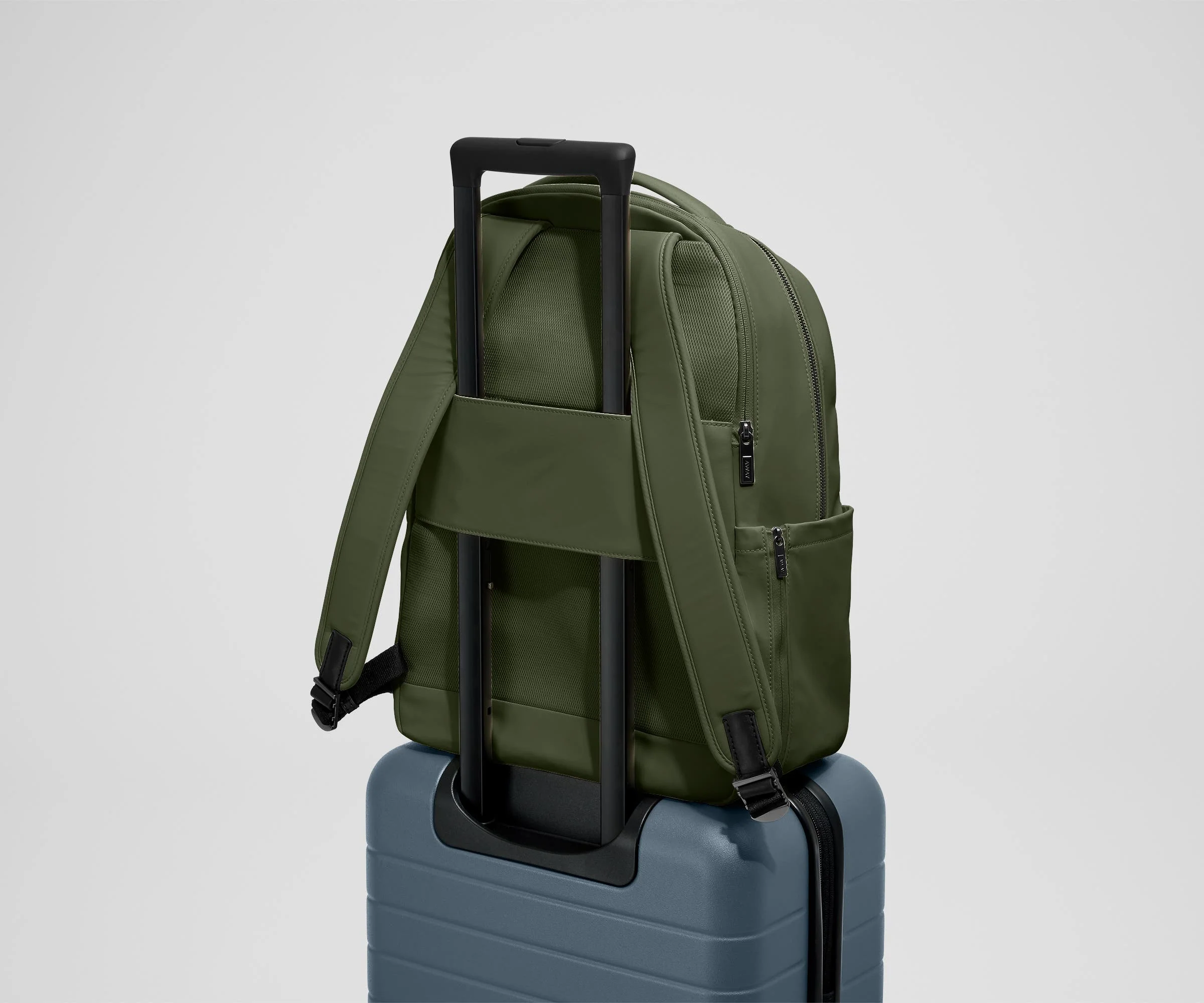 The Commuter Backpack on top of an Away suitcase, attached by the trolley pass-through sleeve