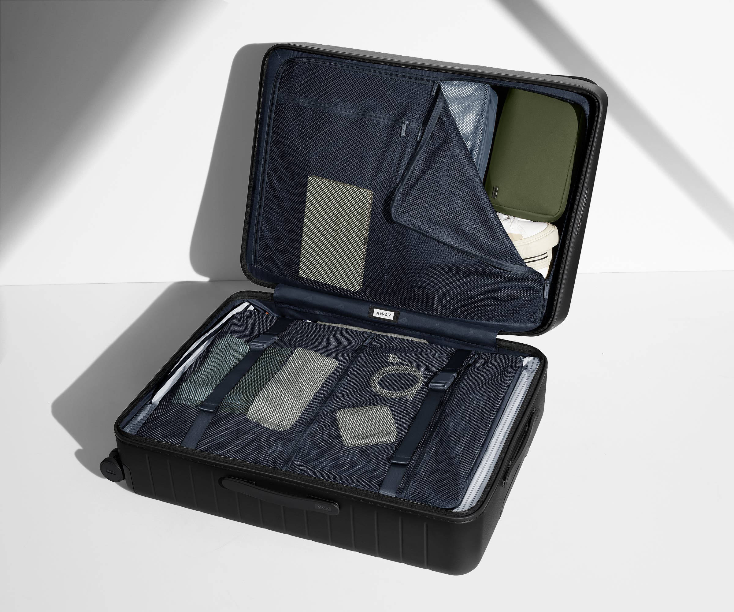 The Medium suitcase in Jet Black shown open on its side and packed with Away's packing organizers to show capacity and the interior compression system, designed to help you pack more in