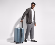 Male-presenting person standing next to a Medium Flex suitcase for scale