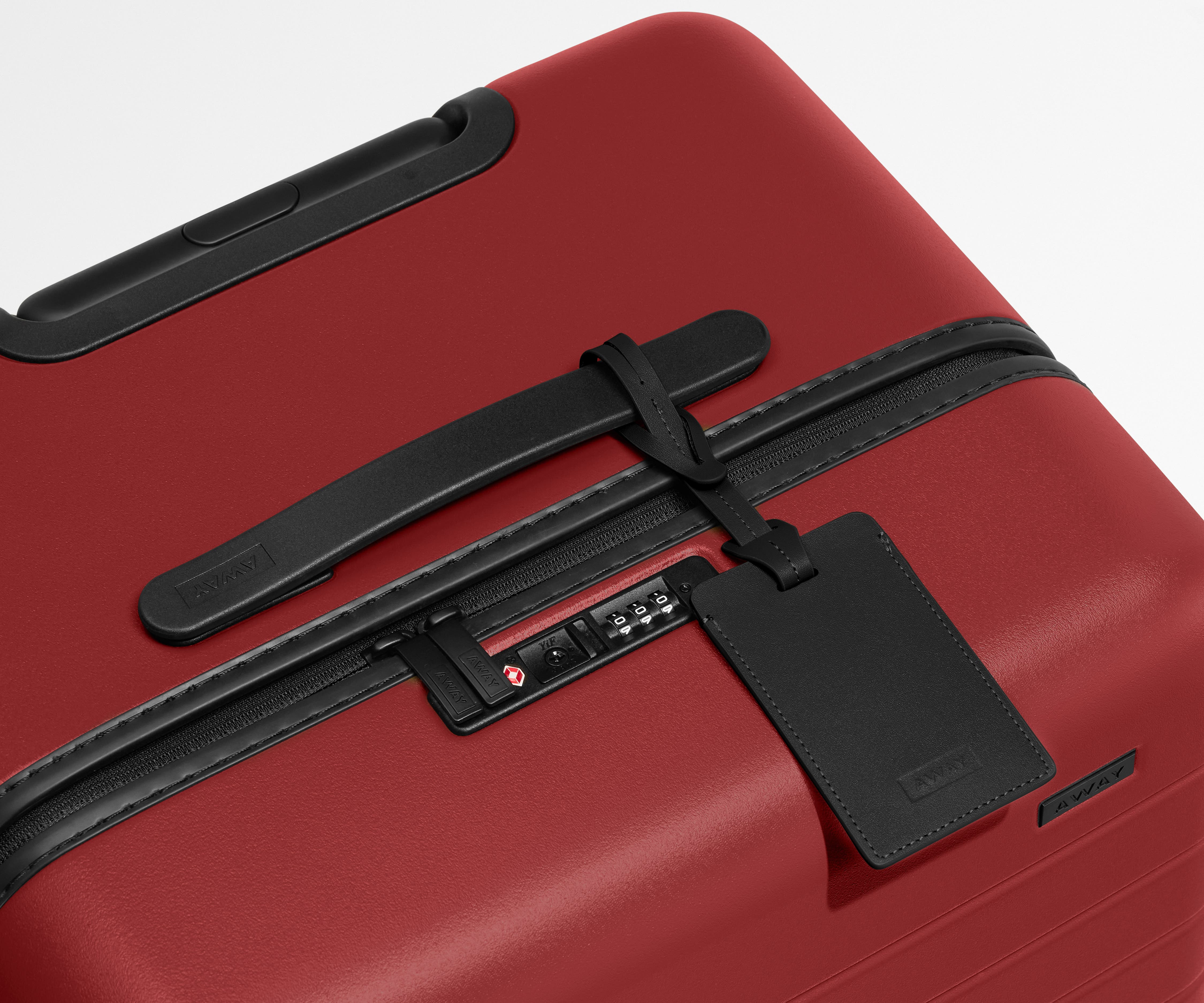 The Trunk suitcase in Tango Red shown shown from above highlighting TSA-approved combination lock and recycled leather luggage tag