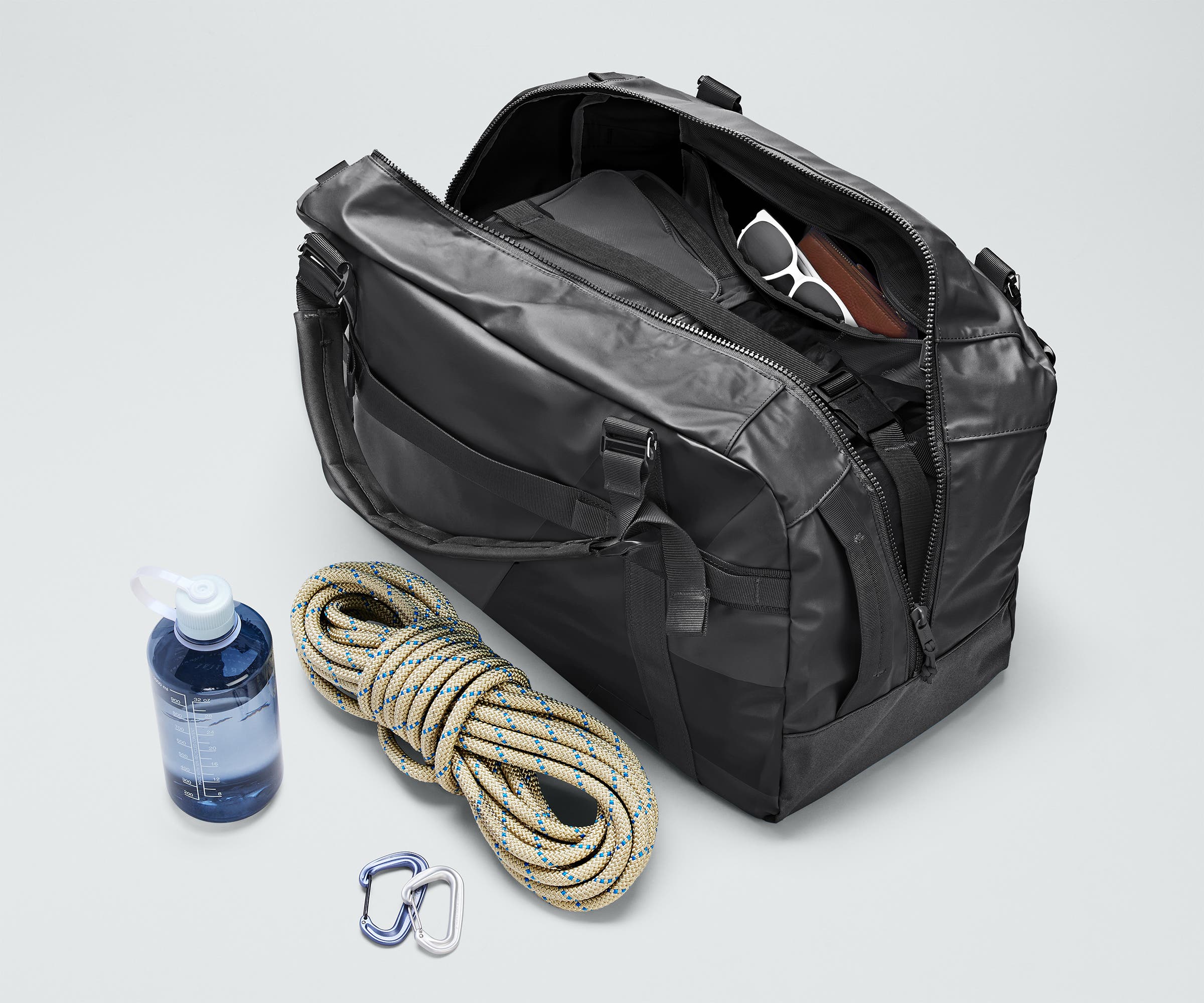 Active Duffle 55L packed with travel essentials and outdoor gear including a packing cube, sunglasses, wallet, carabiner and rope, and water bottle
