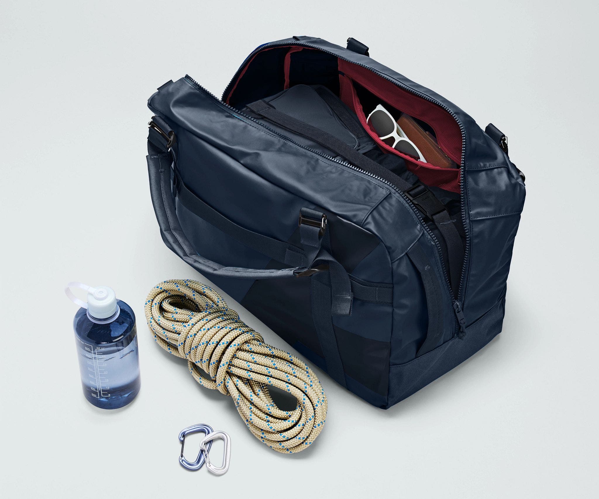 Active Duffle 55L packed with travel essentials and outdoor gear including a packing cube, sunglasses, wallet, carabiner and rope, and water bottle
