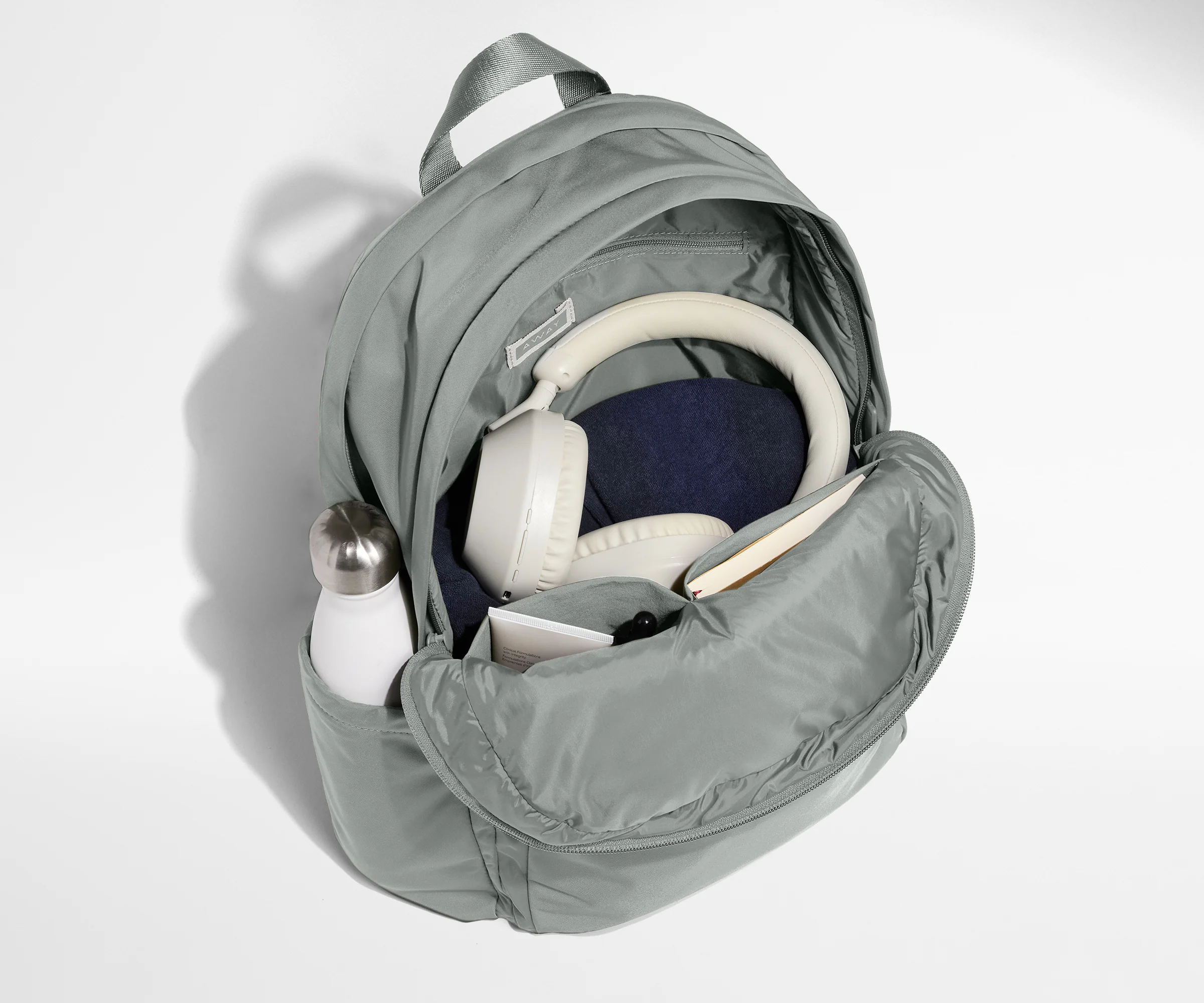 Gray backpack with items like a water bottle and jeans on a white background