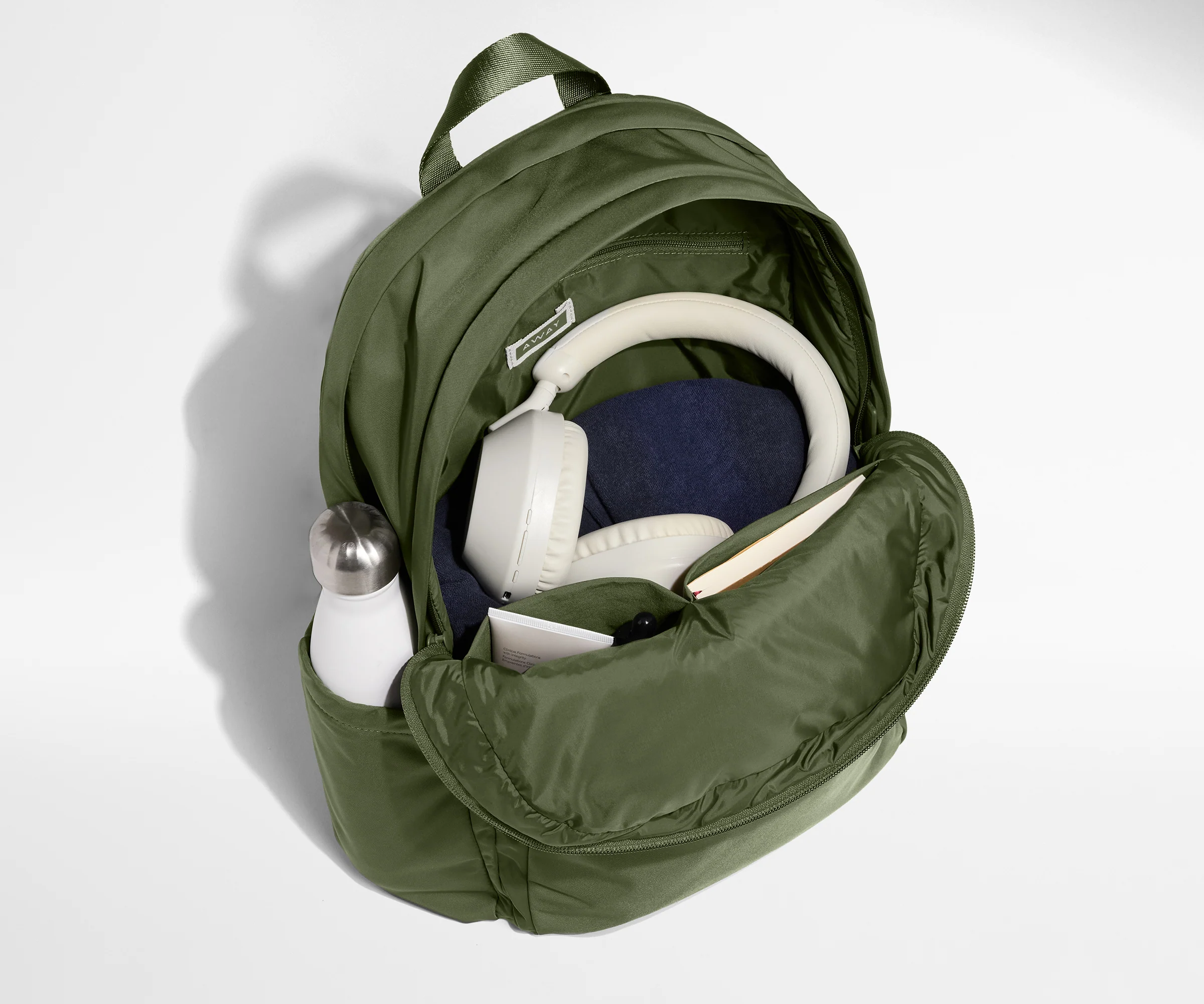 Green backpack with items like a bottle, mask, and headphones on a light gray background