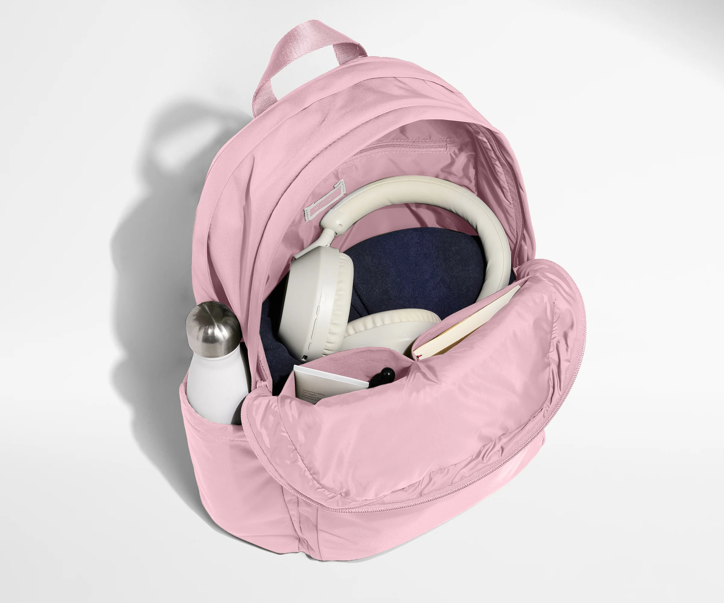 Pink backpack with a water bottle, denim item, and gray strap on a light gray background
