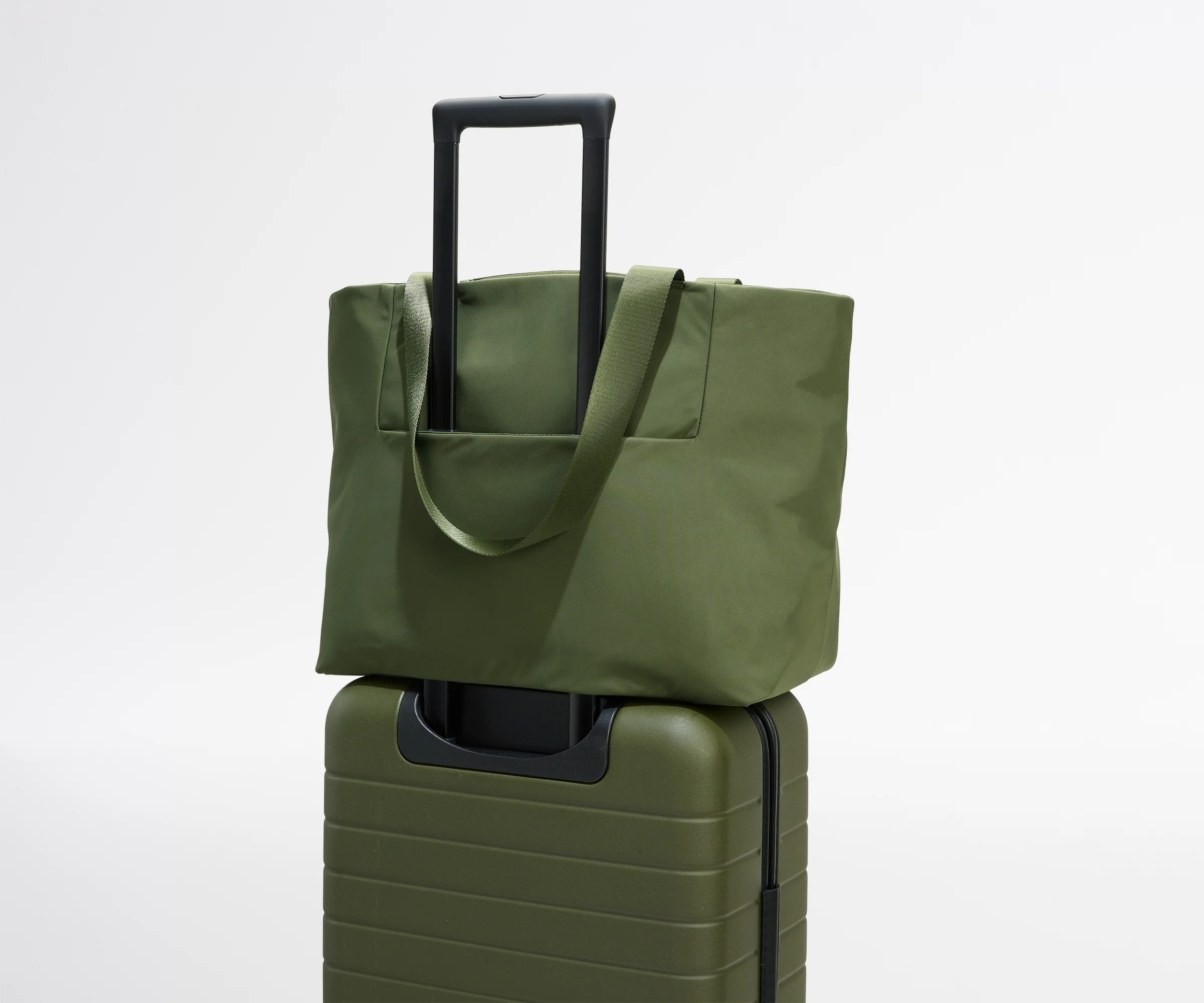 Green tote bag on top of a green suitcase against a white background