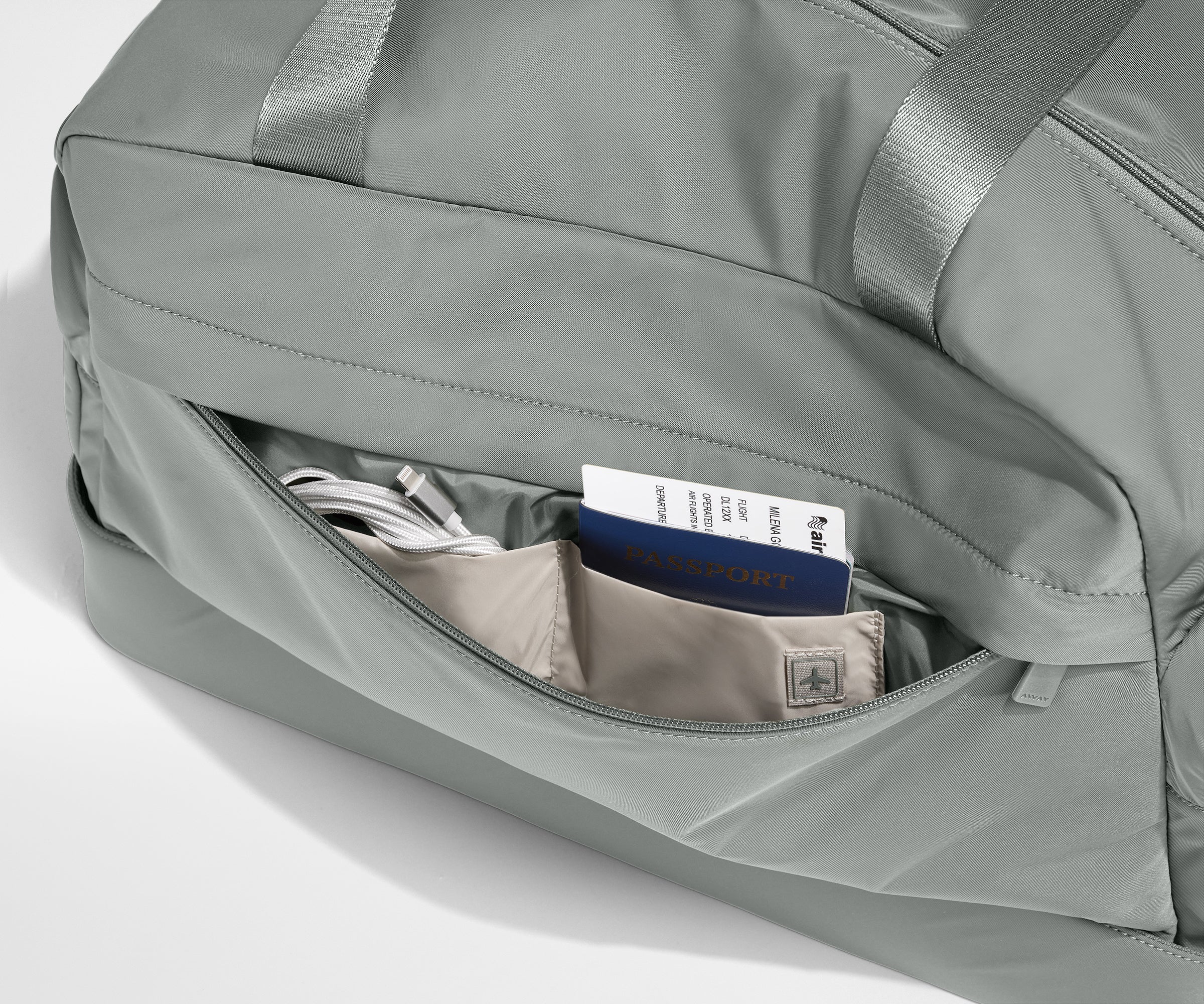Gray duffel bag with a pocket containing a passport and phone on a light gray background