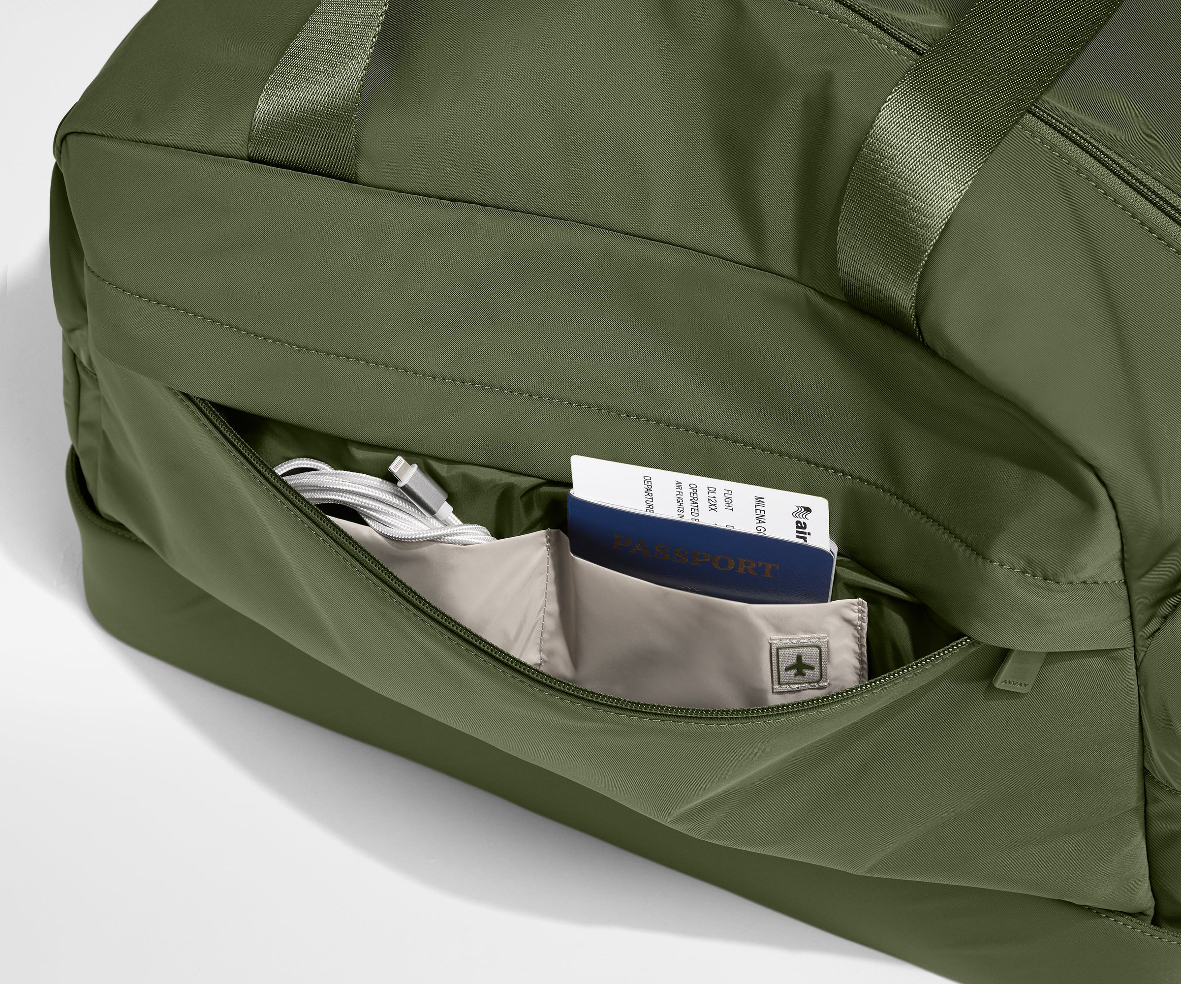 Green duffel bag with a pocket containing a passport and phone on a light gray background