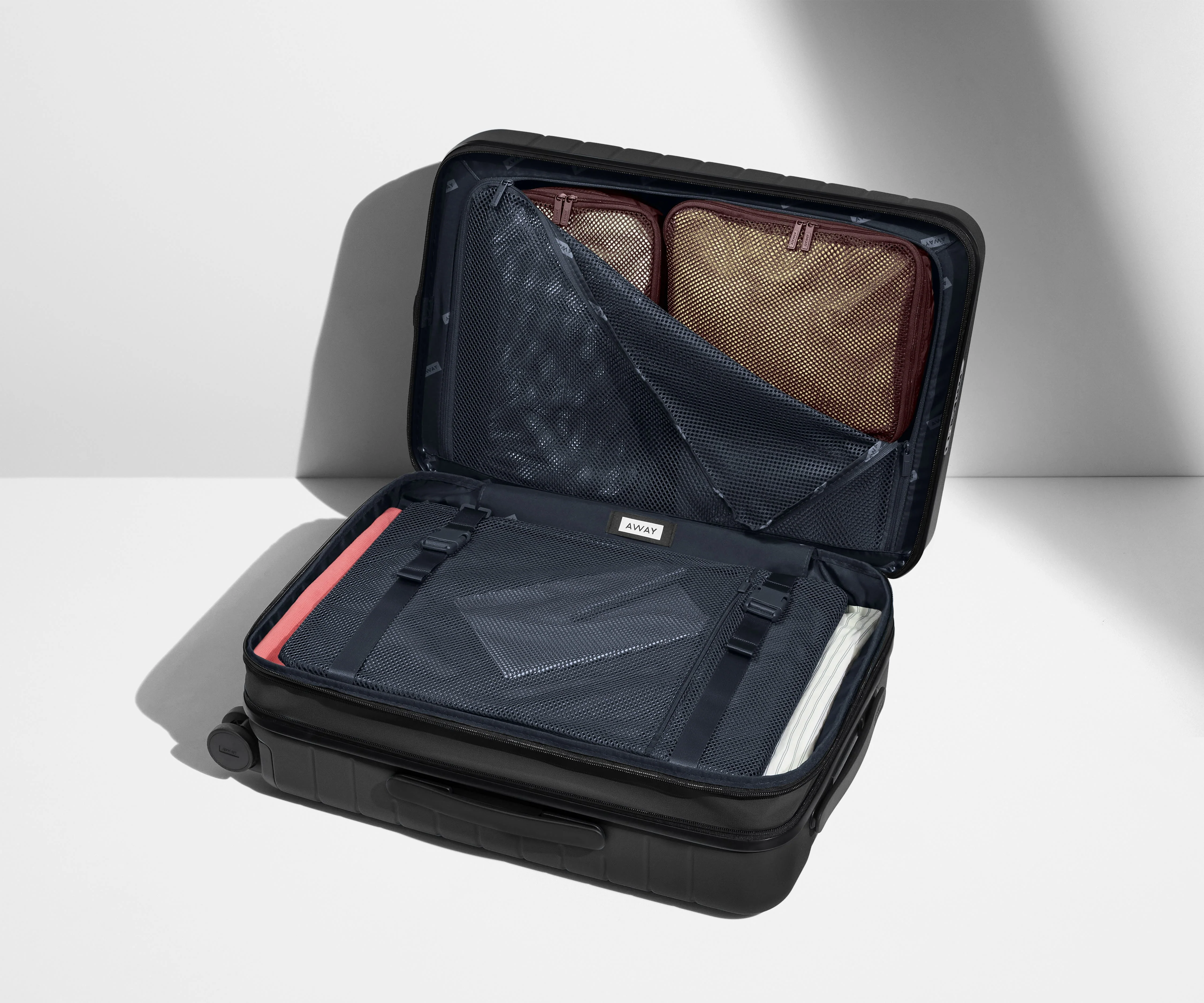 The Carry-On Flex suitcase in Jet Black shown open on its side and packed with Away's packing organizers to show capacity and the interior compression system, designed to help you pack more in