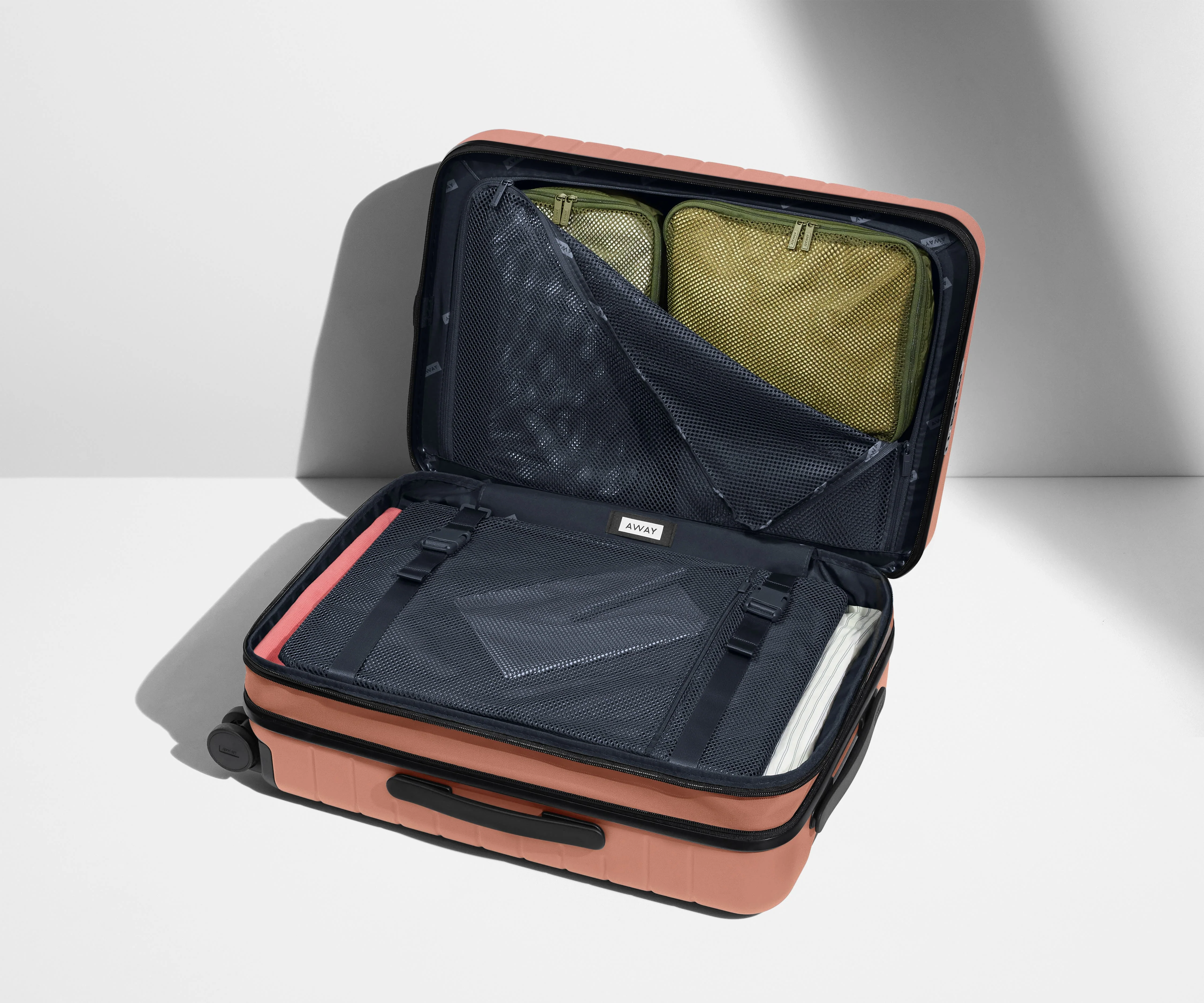 The Bigger Carry-On Flex suitcase in Clay Pink shown open on its side and packed with Away's packing organizers to show capacity and the interior compression system, designed to help you pack more in