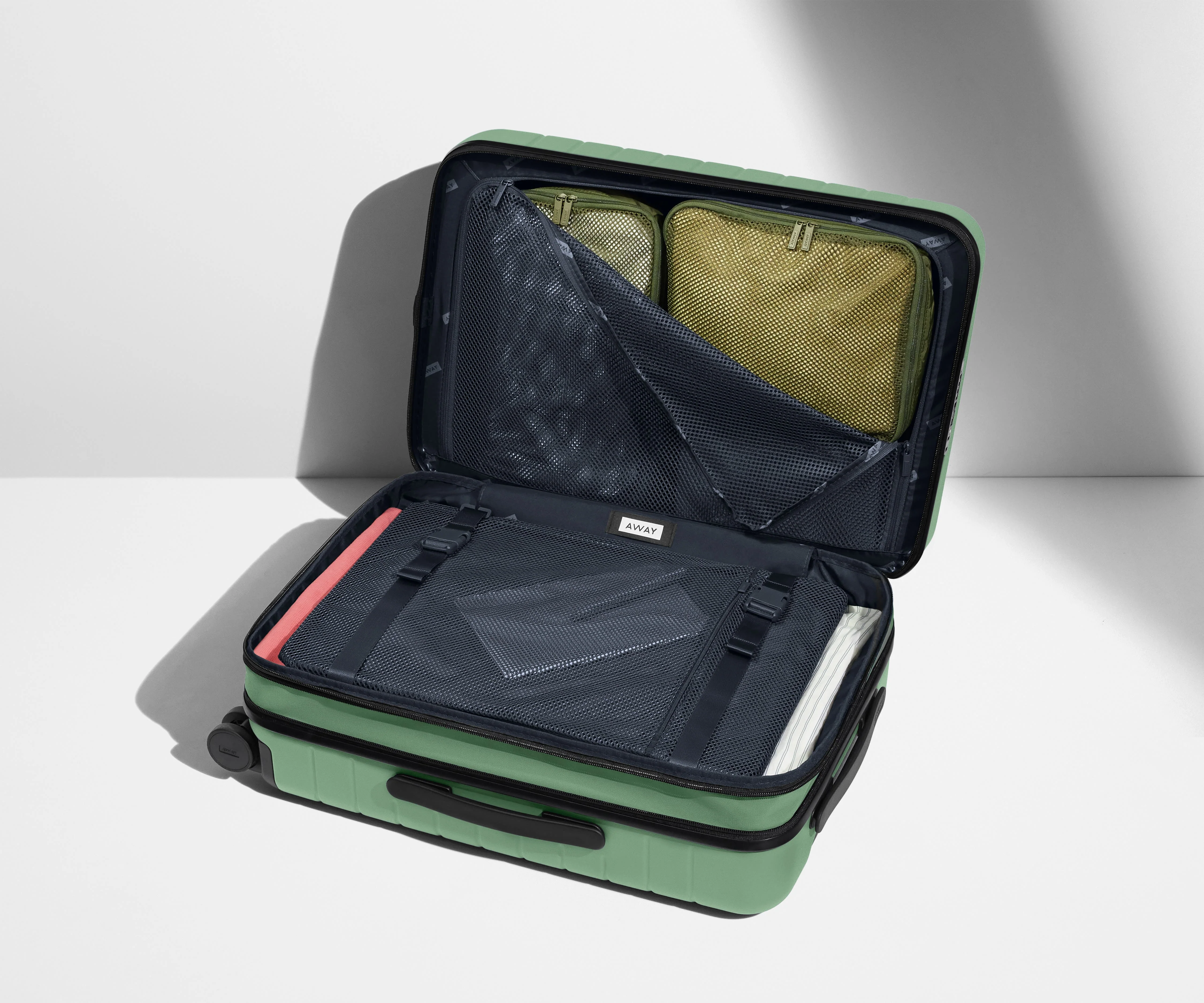 The Bigger Carry-On Flex suitcase in Sea Green shown open on its side and packed with Away's packing organizers to show capacity and the interior compression system, designed to help you pack more in