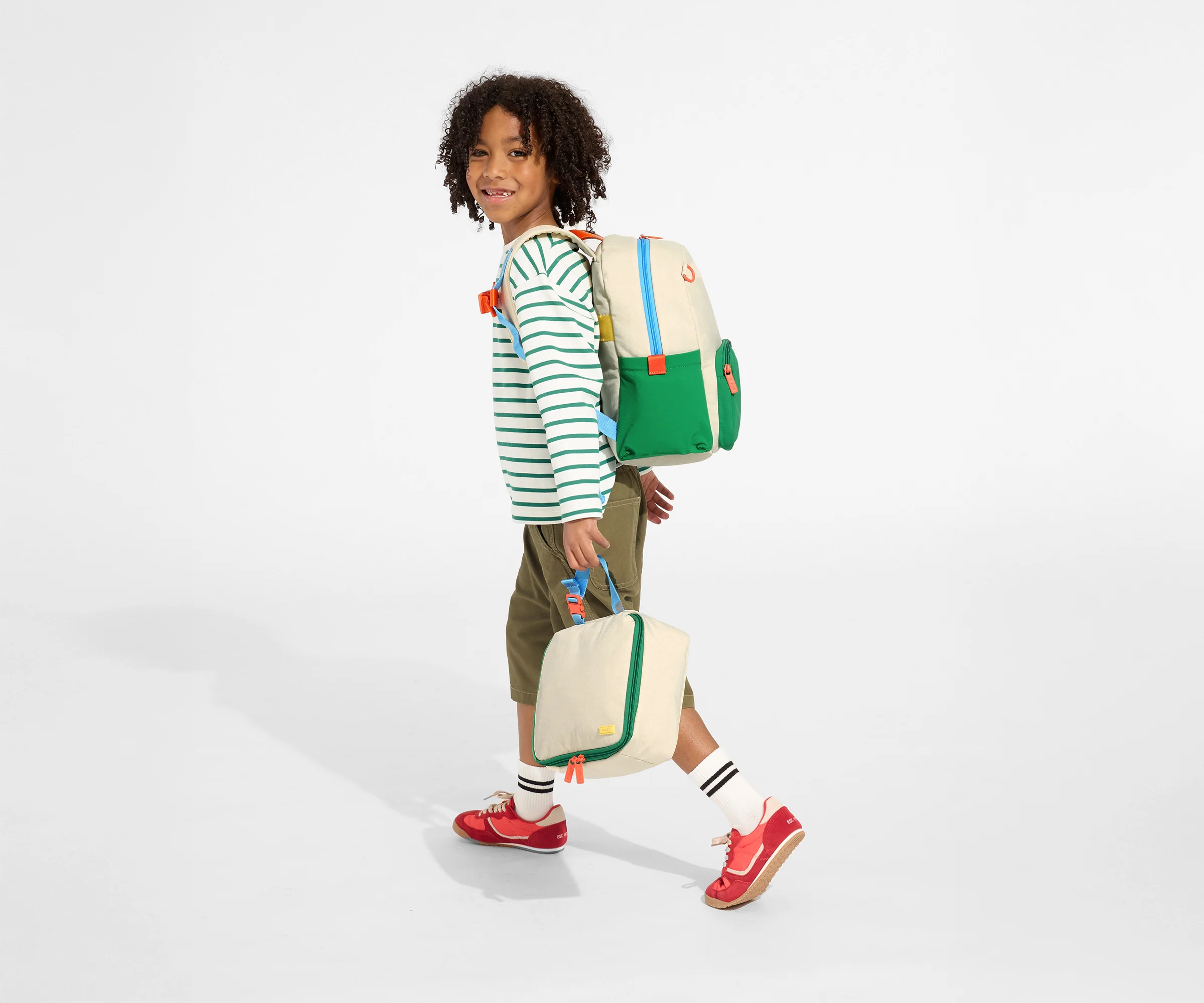 A child model wearing the Kids Backpack in Marshmallow White with the chest strap in use and holds the Kids Lunch Box in Marshmallow White // Daniel, age 8, wears the Kids Backpack in Marshmallow White and holds the Kids Lunch Box in Marshmallow White.