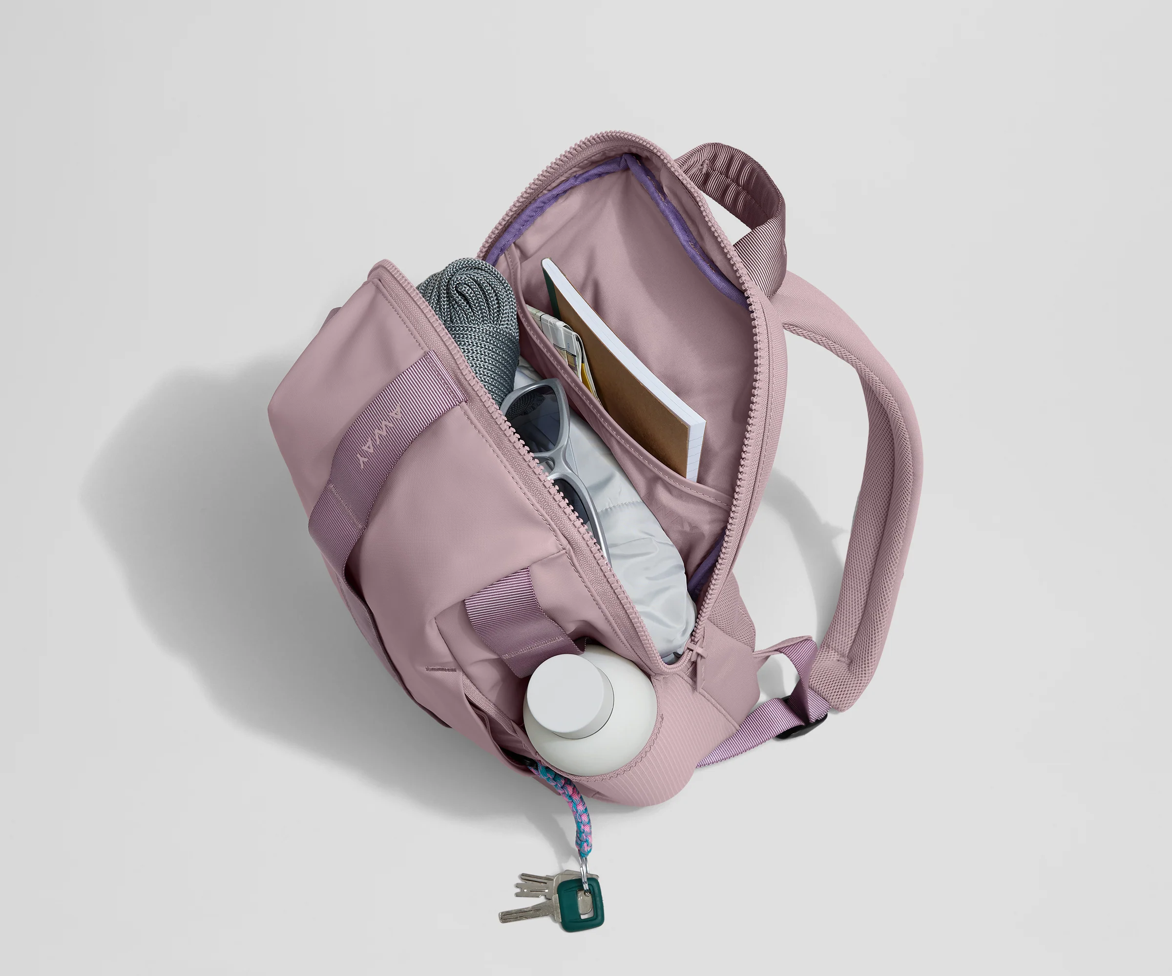 Daypack packed with a light jacket, sunglasses, notebook, map, and other travel gear. Water bottle featured in the exterior water bottle pocket.
