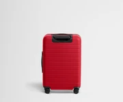 Red suitcase with black handle and wheels on a light gray background