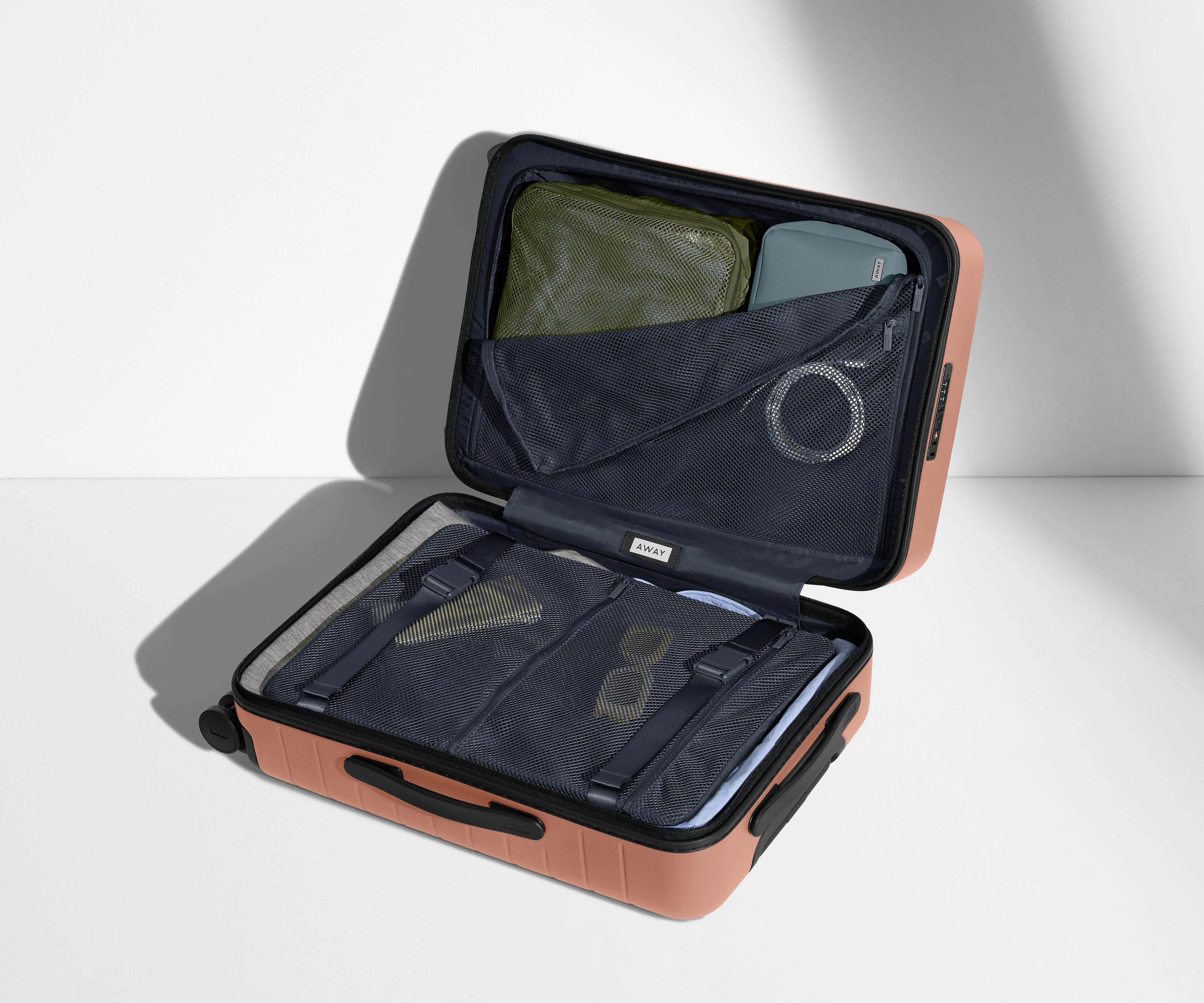 The Bigger Carry-On suitcase in Clay Pink shown open on its side and packed with Away's packing organizers to show capacity and the interior compression system, designed to help you pack more in