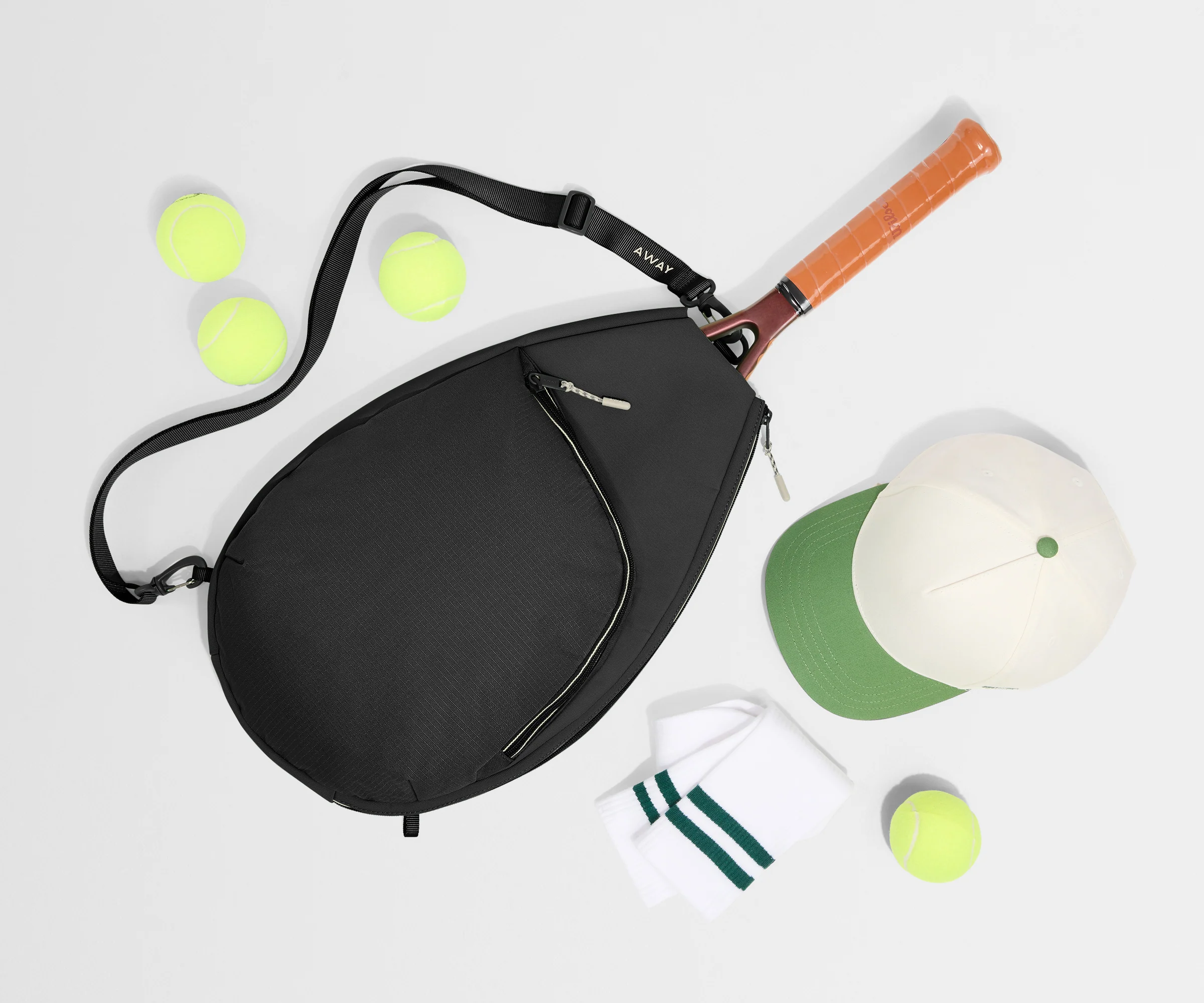Black bag with a tennis racket, balls, and a cap on a light gray background