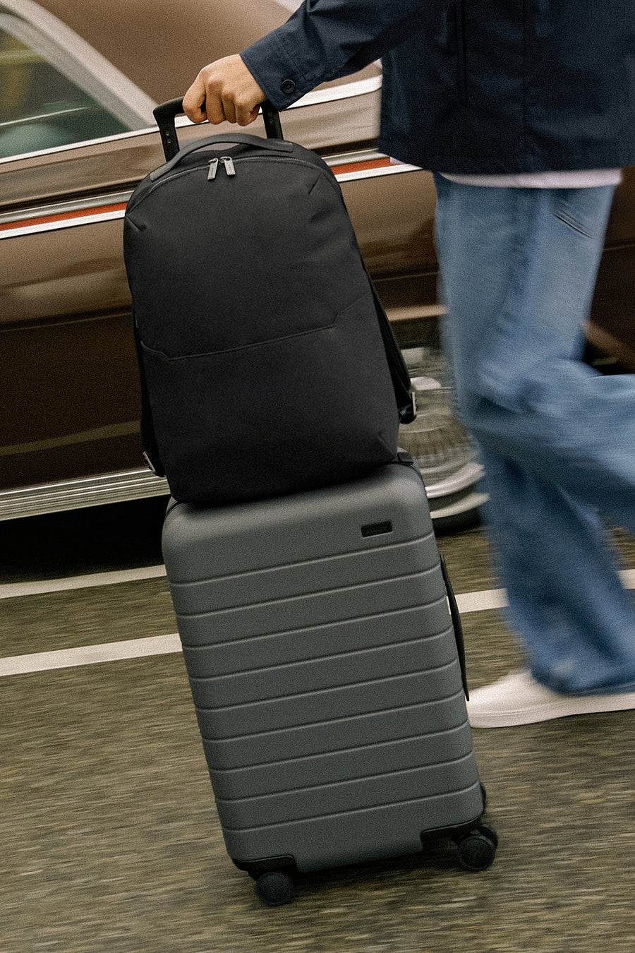Person holding a black suitcase on top of a suitcase in an airport setting.