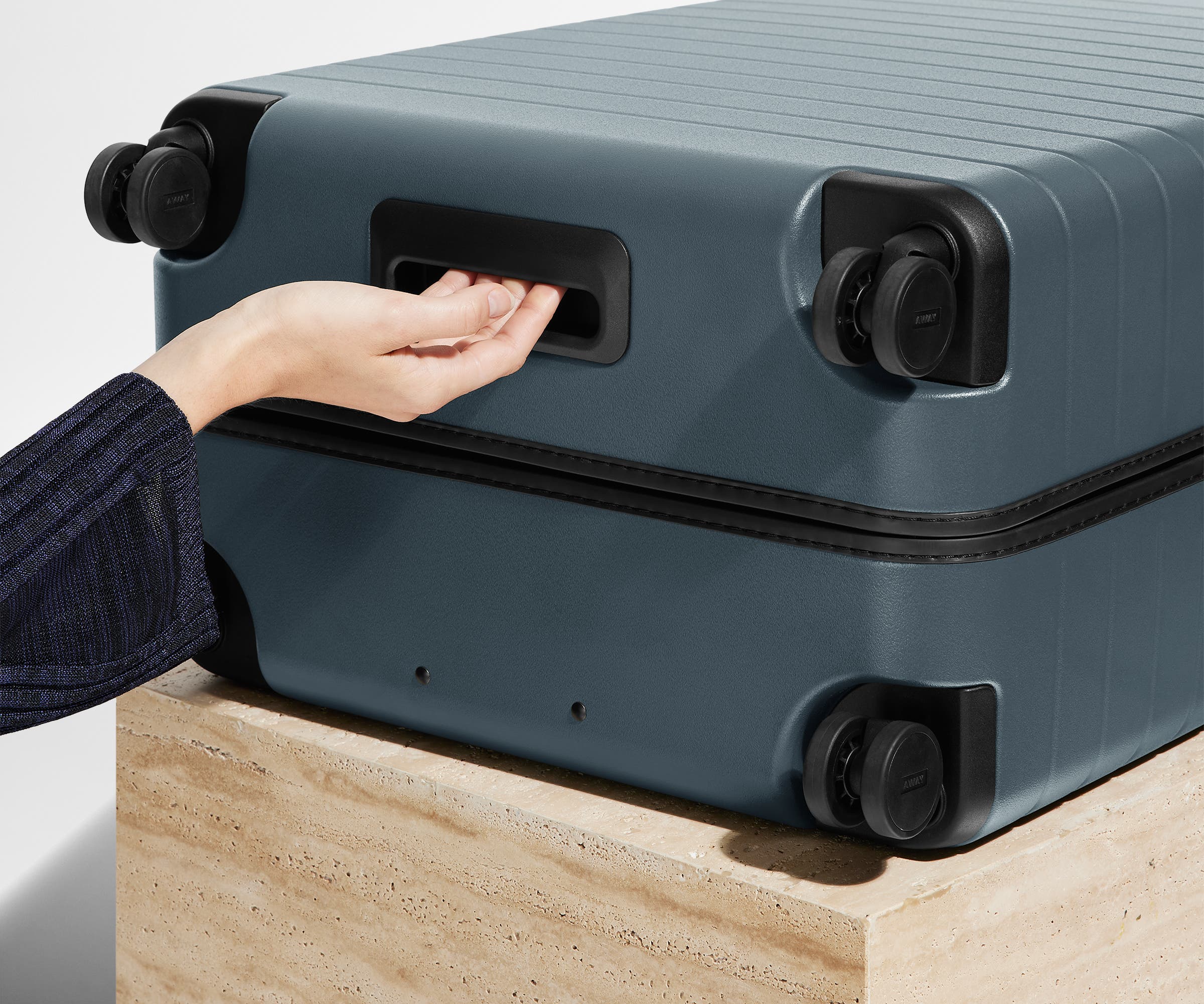 The Large suitcase in Coast Blue shown from below highlighting the underside grab handle