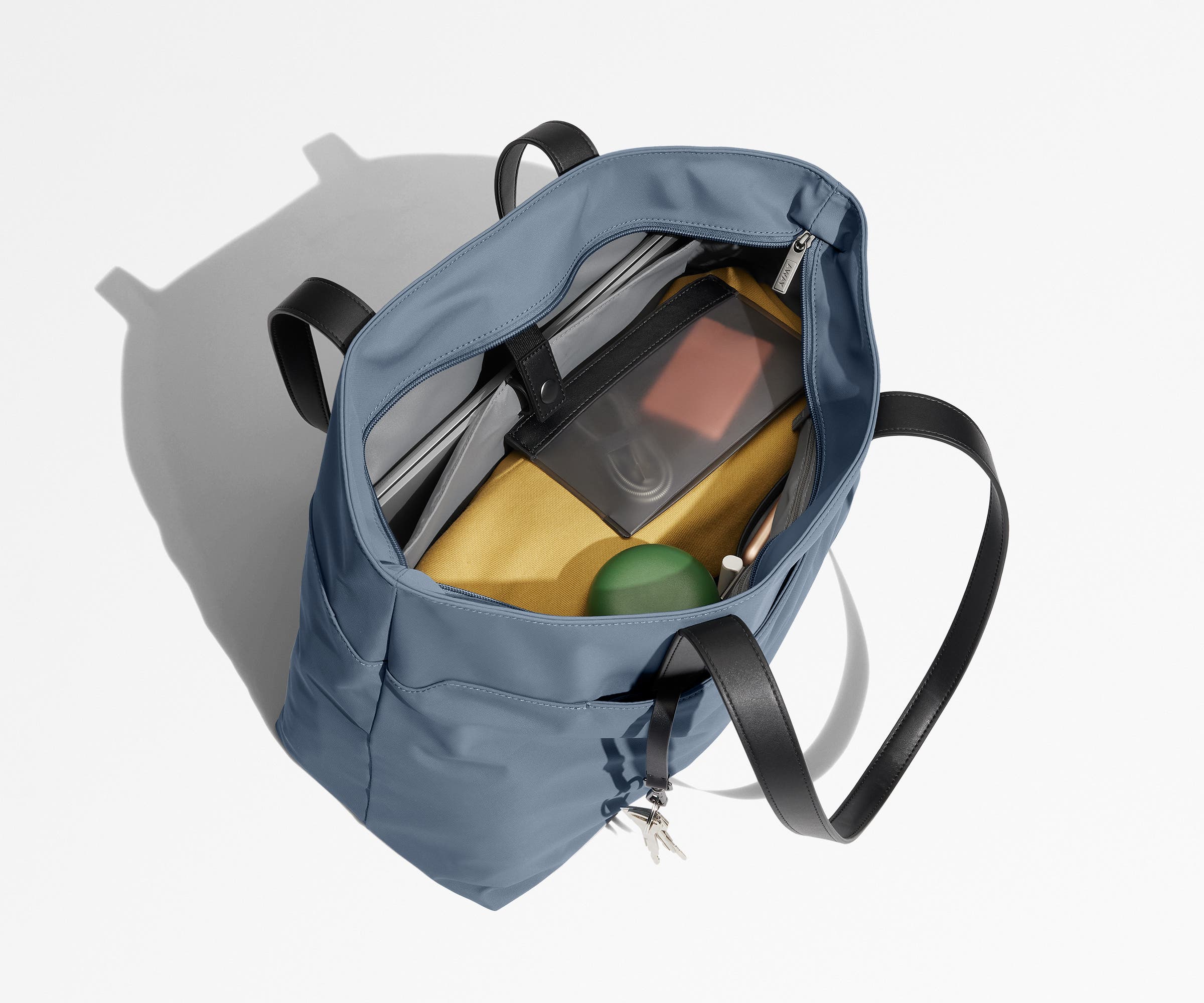 Tote bag packed with a laptop, water bottle, travel pouch, and sweater. A key is attached to the hidden key leash