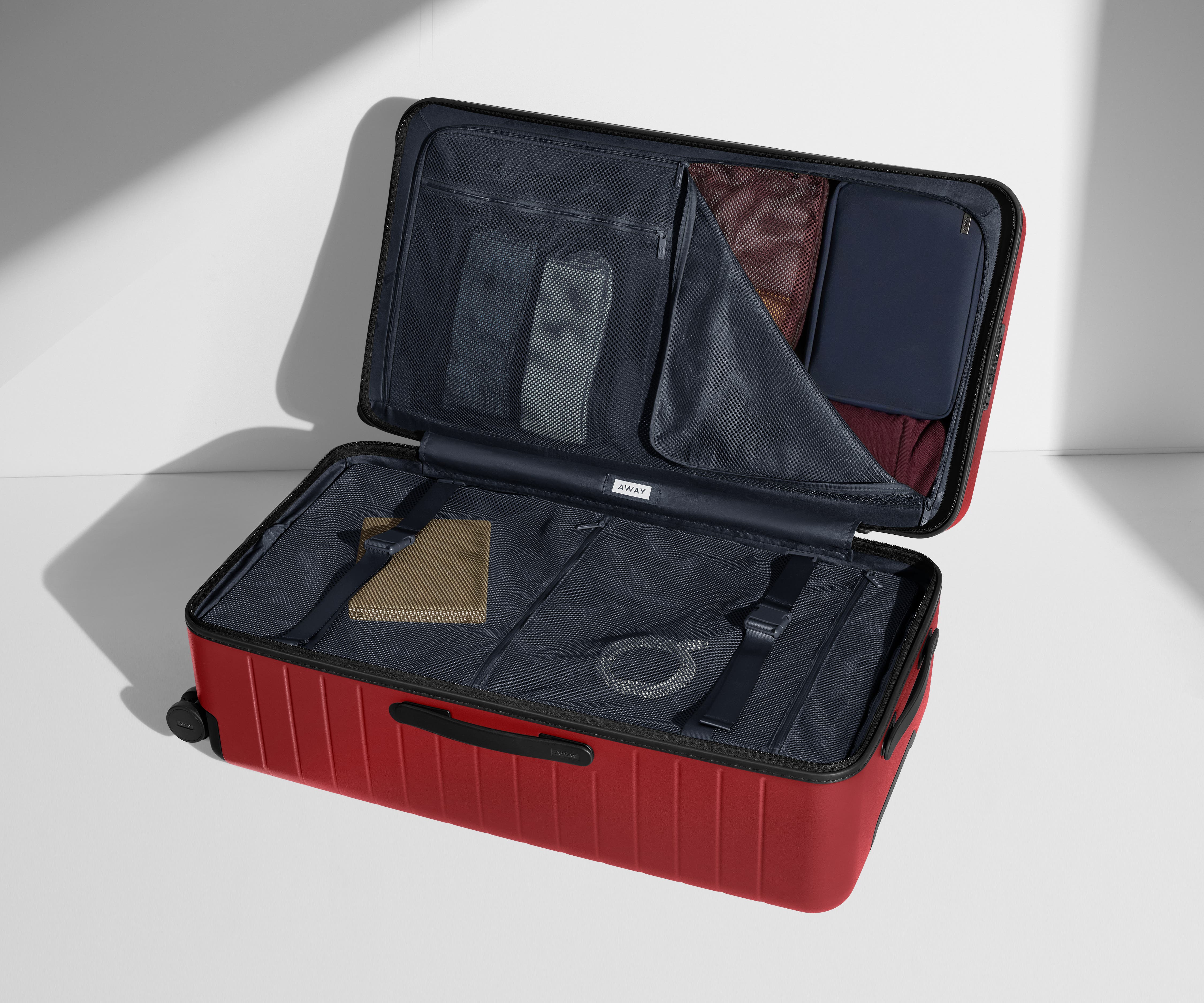 The Trunk suitcase in Tango Red shown open on its side and packed with Away's packing organizers to show capacity and the interior compression system, designed to help you pack more in