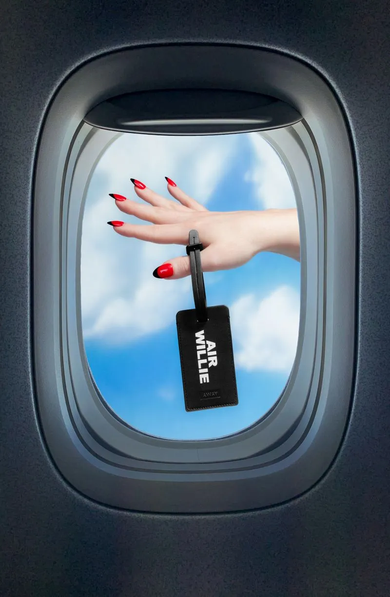 a woman holding an Away luggage tag outside of a plane window with clouds in the background