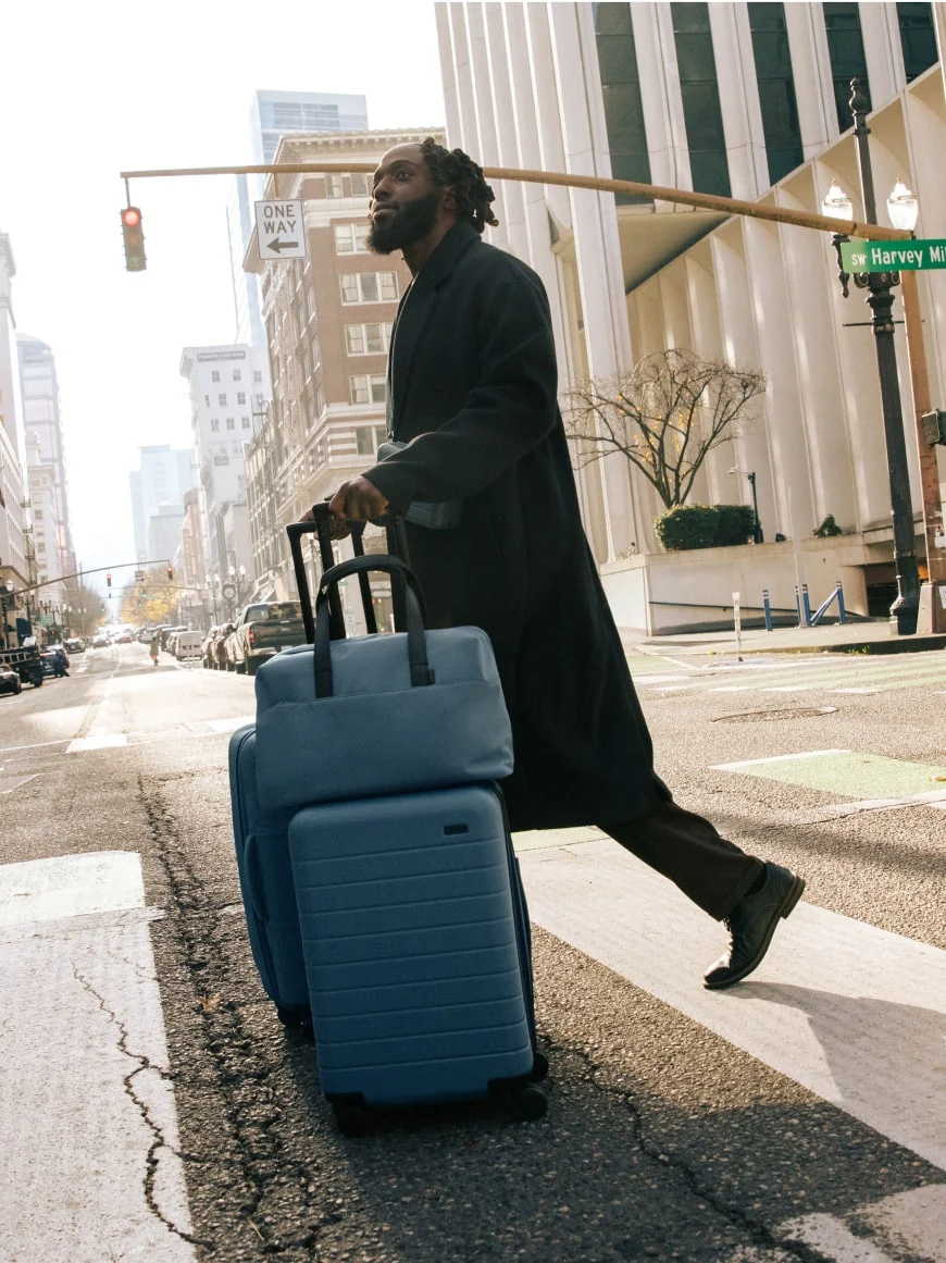 A man exploring the streets of Portland with The Carry-On, The Everywhere Bag, and The Softside Medium -- all in Coast Blue.