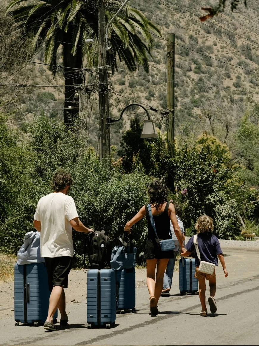 A family of three walking on a lush road with a set of Away suitcases in blue