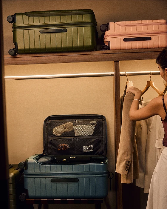 Green and pink suitcase on a shelf with an open blue suitcase in a hotel environment
