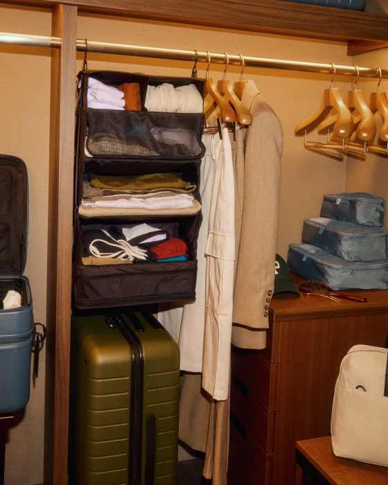 Closet with hanging clothes, folded items, and a suitcase.